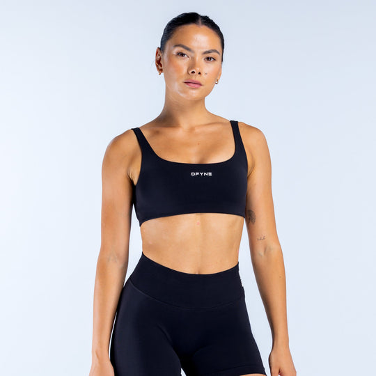 Black scoop-back sports bra with wide straps and DPYNE logo on front.