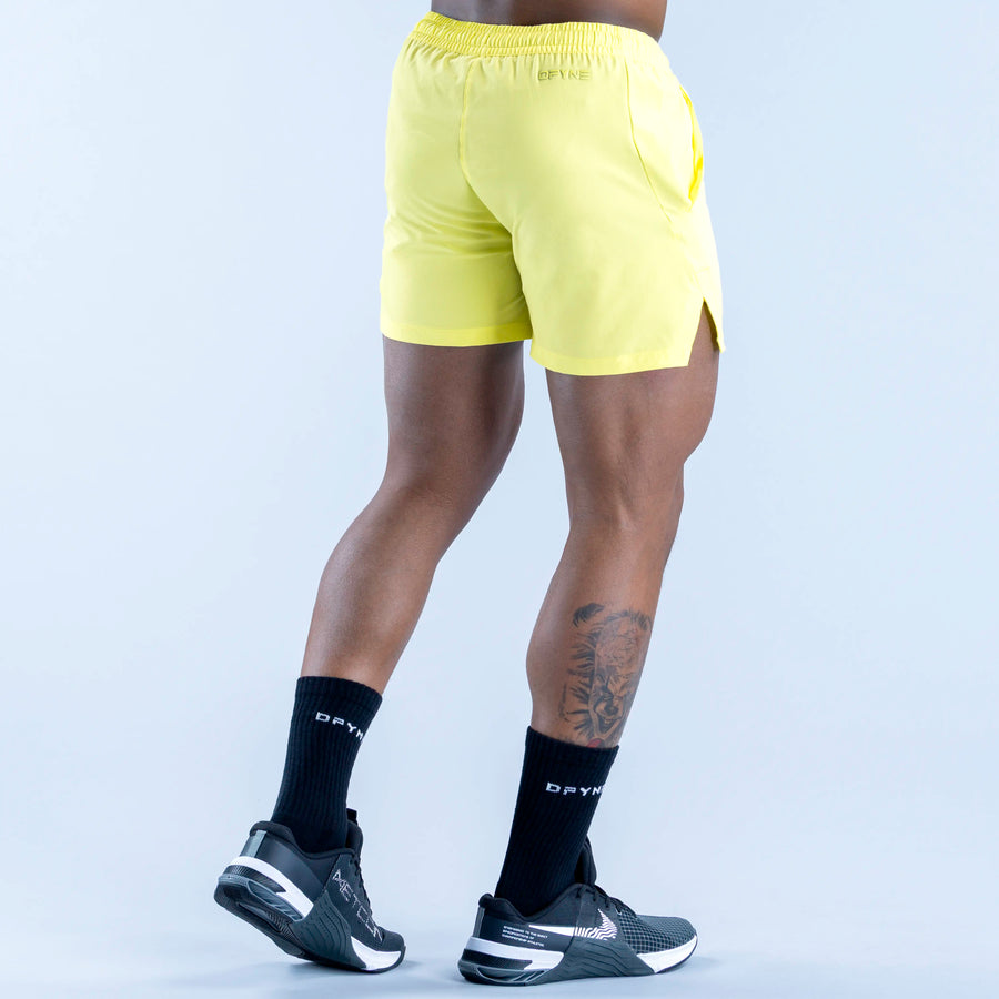 Lime yellow training shorts, rear three-quarter view, elastic waistband, mid-thigh