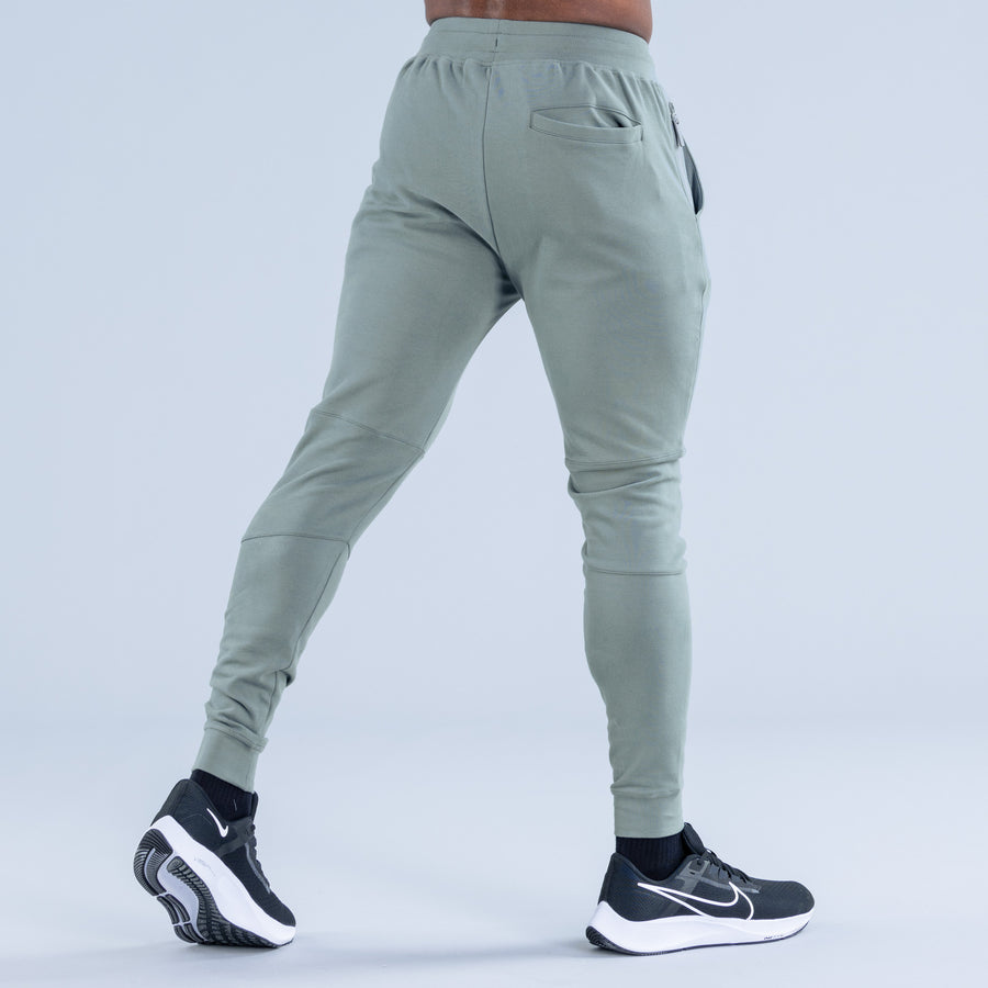 Sage green tapered jogger pants from back, slanted pockets and elastic cuffs