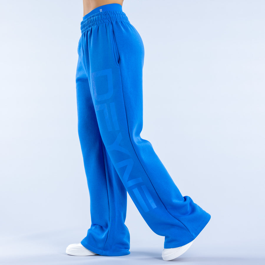 Blue wide-leg joggers, side view, elastic waistband and stacked graphic on leg