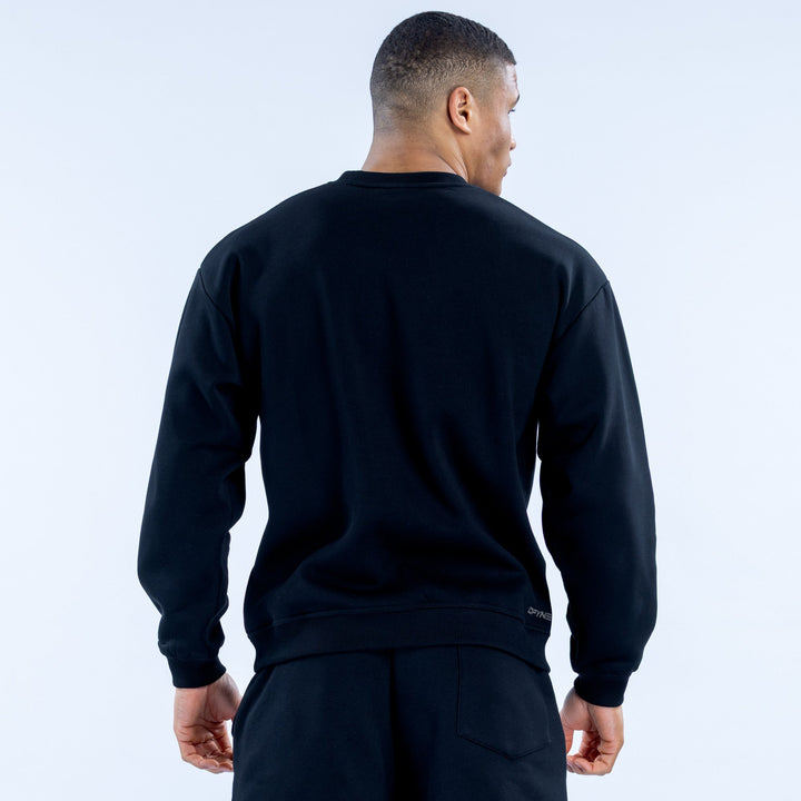 Black crewneck sweatshirt, back view with ribbed hem and small logo patch