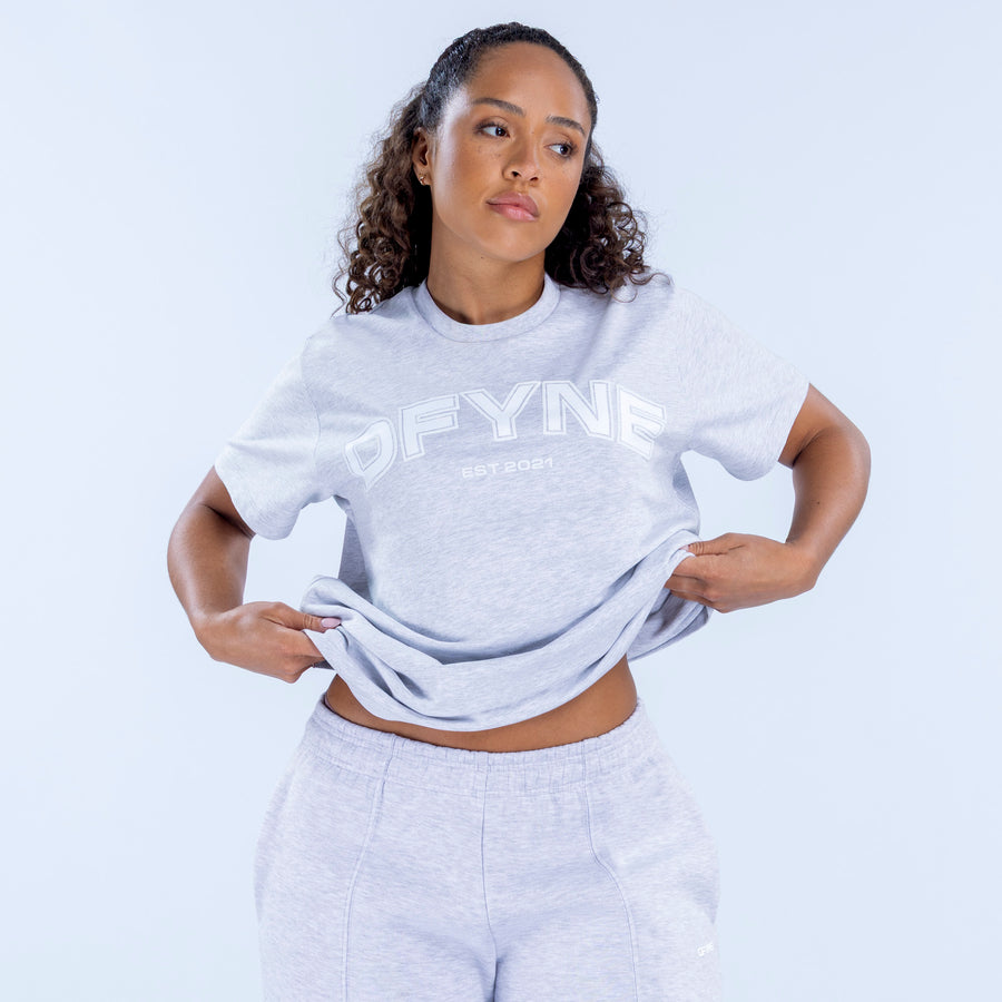 Light gray oversized graphic tee with front logo graphic, cropped waist view