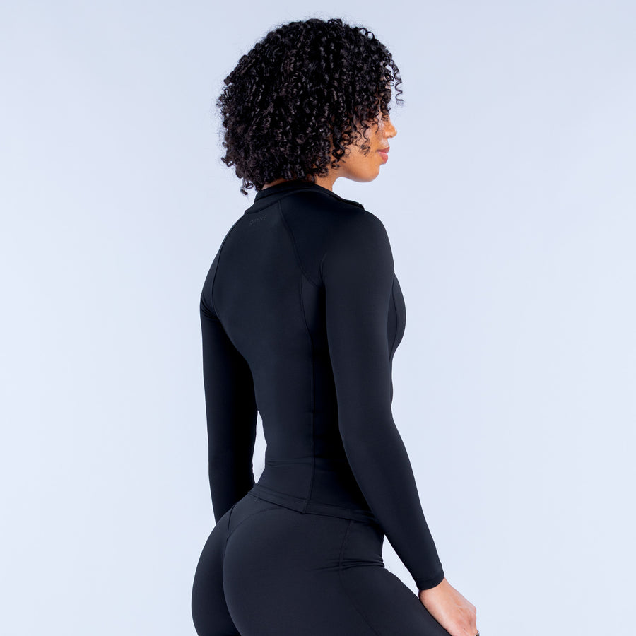 Fitted black long-sleeve zip-up athletic top, side view, front zipper and seams