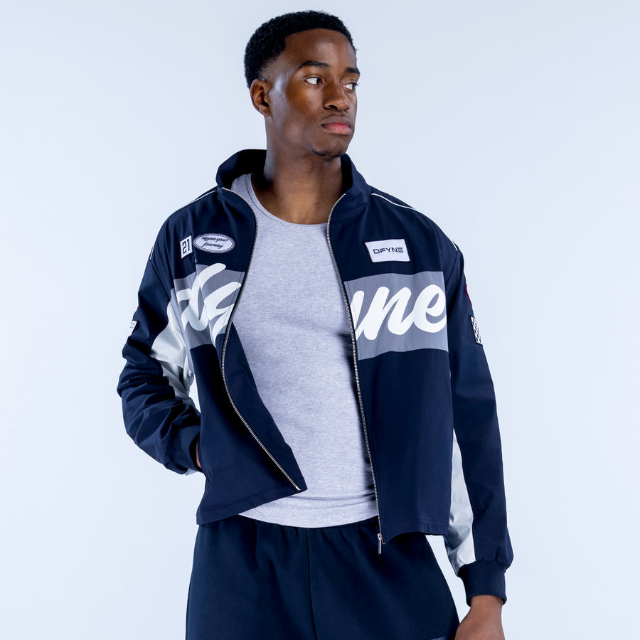 Two-tone track jacket with full zipper; navy jacket with gray panel, worn open over a tee