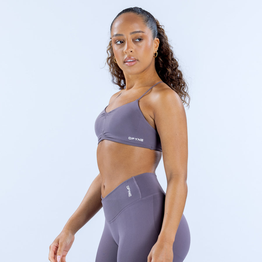 Women's purple racerback sports bra with matching logo label at center chest