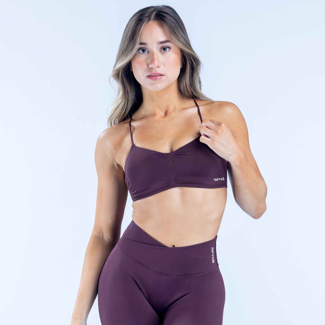 Plum sports bra with thin spaghetti straps and small printed logo at hem